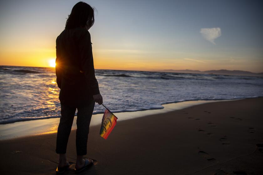 LOS ANGELES, CA - MARCH 05: Eliza, a junior at University of California, Berkeley, is photographed with a pride flag from Gender Equity on campus, at the beach near Los Angeles, CA, Friday, March 5, 2021. Eliza, who is out as gay while at school, has not come out at home and has chosen to have her identity obscured. (Jay L. Clendenin / Los Angeles Times)