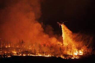 A night flying helicopter drops water on flames as the Thompson Fire burns, Tuesday, July 2, 2024, in Oroville, Calif. (AP Photo/Ethan Swope)