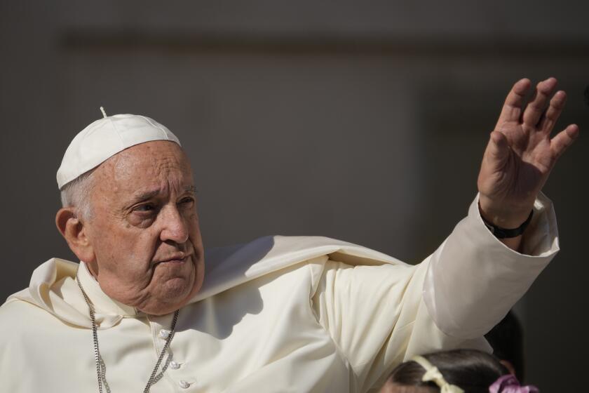 Pope Francis in a white robe and white cap holding up his left hand