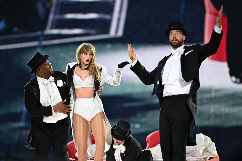 Taylor Swift performing onstage and is joined by Travis Kelce in a top hat and tuxedo